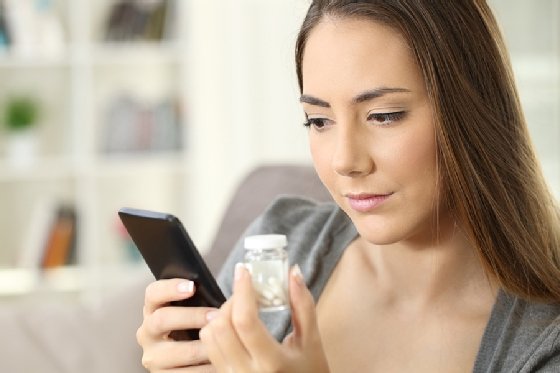 A patient holds a bottle of medication while looking up information on her phone.
