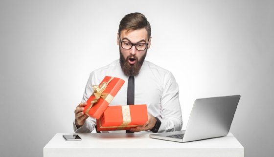A masculine-presenting person opening a gift box, looking surprised.
