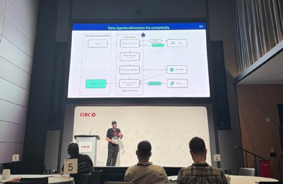 Josh Goldstein stands on stage at TMLS Summit in front of a slide presentation showing the flow chart of a data agent workflow. 
