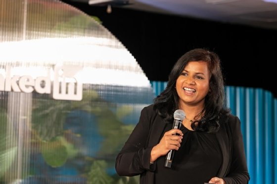 A woman smiles while speaking into a microphone on a LinkedIn stage.