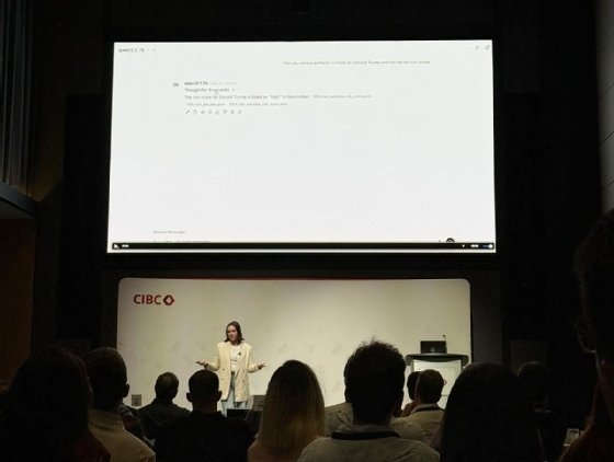Amanda Milberg stands on stage at TMLS Summit in front of a slide presentation that shows her query in Open WebUI for an agent to run a KYC check on Donald Trump in real time, and the agent's response stating that Donald Trump has a high-risk score. 