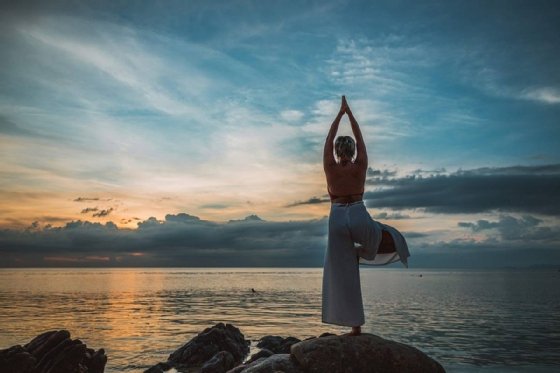 A woman performs a yoga pose while overlooking a lake.